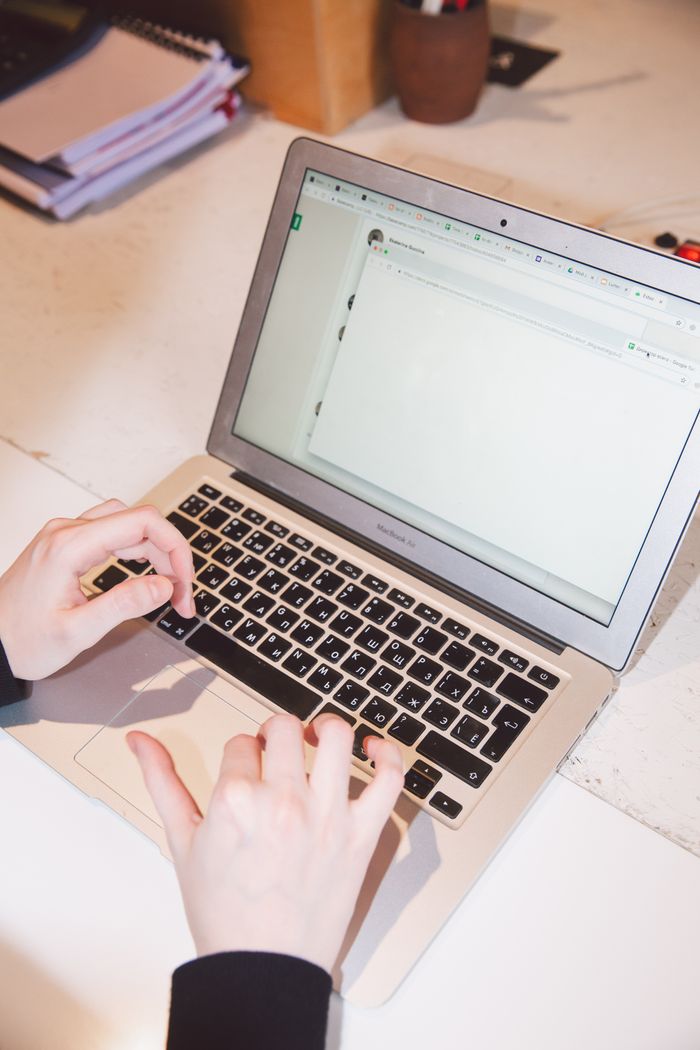 Gros plan sur des mains tapant sur un ordinateur portable posé sur un bureau de travail, évoquant l’activité professionnelle ou la communication en ligne.